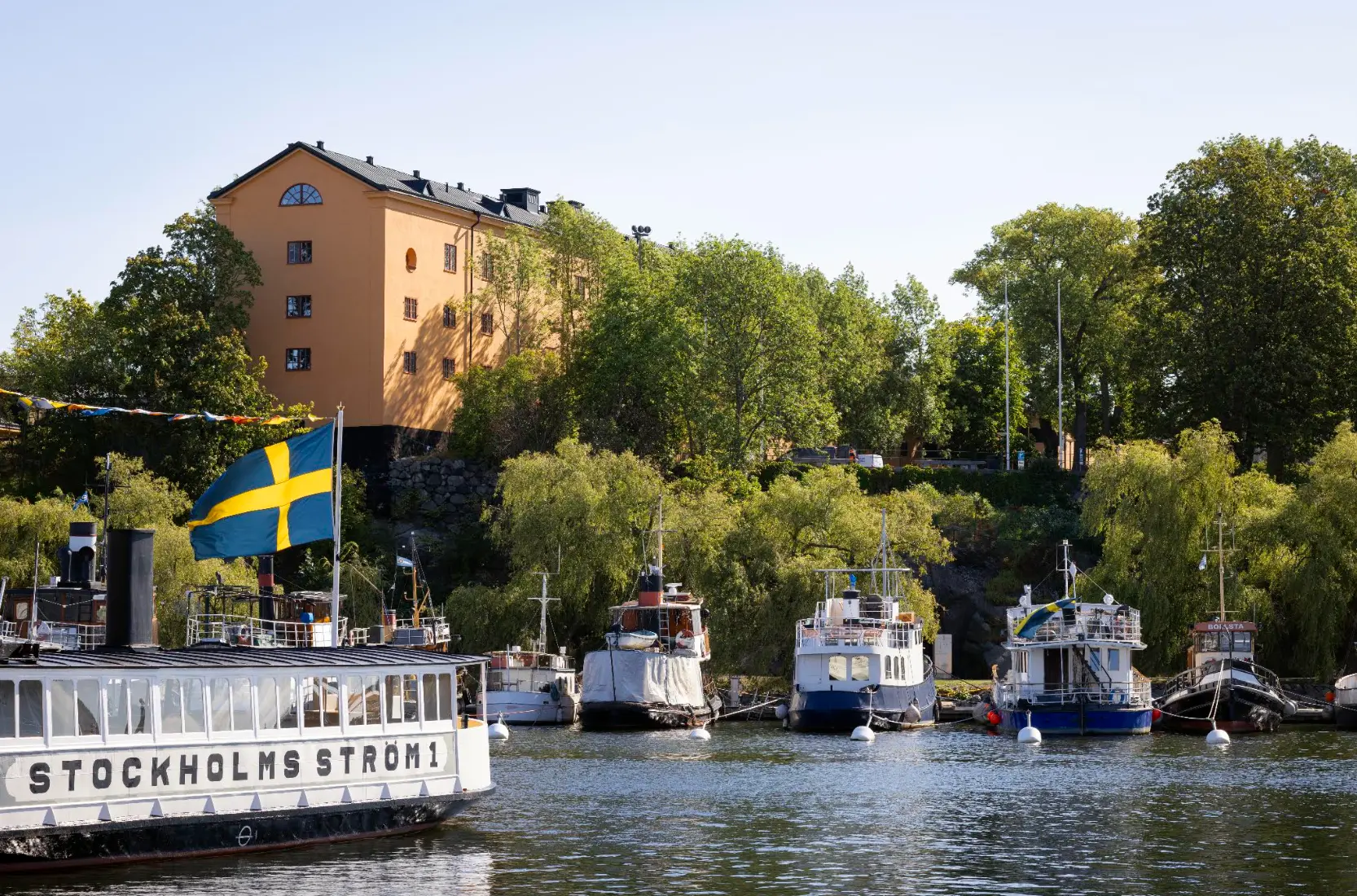 Tyghuset sett från vattnet på Skeppsholmen, omgivet av grönska och båtar